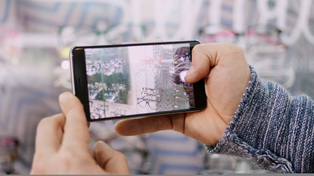 近距离拍摄男性在眼镜零售店、眼镜店拿着智能手机拍眼镜的照片，以便以后在家里看到什么模特买，或分享社交网络图片下载