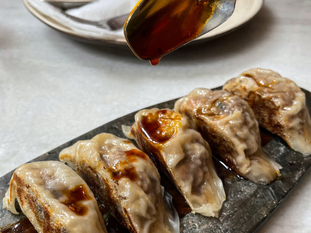 特写图片:勺子将辣椒酱油淋在混合馄饨(中国饺子)上，鸡肉、猪肉或鸭肉放在拼盘上，餐厅餐桌上放置金属叉子，勺子折叠在餐巾纸上，重点放在前景图片下载