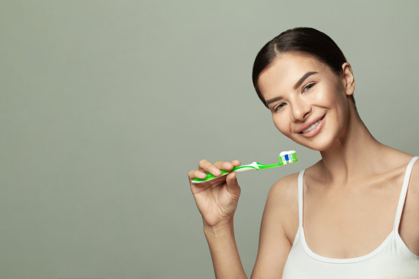 一个微笑可爱的女人的肖像持有牙刷在浅绿色的背景图片下载