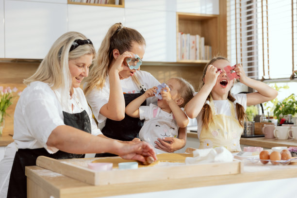 年轻的母亲和女儿拿着饼干刀具和眼镜奶奶手里拿着擀面杖擀面团。家庭烘焙烹饪美味的圣诞早餐饼干。玩得开心图片下载