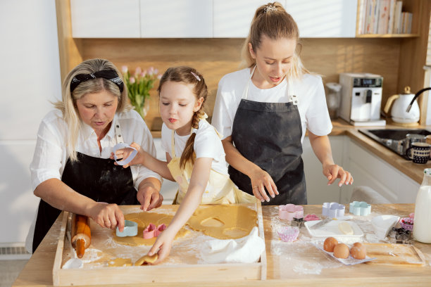 可爱的孙女手里拿着心形的饼干切割机，帮奶奶切饼干。家庭参与过程烘焙烹饪现代漂亮的厨房图片下载