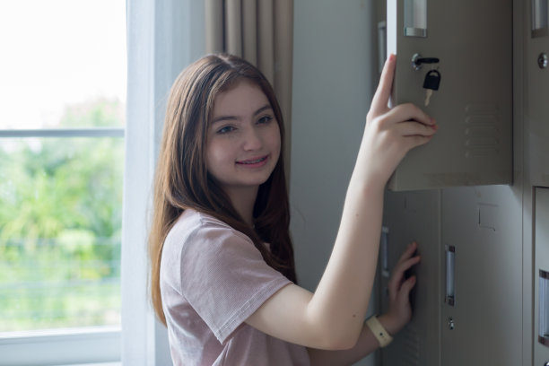 一个学生在学校打开她的储物柜。一个女学生微笑着打开她的储物柜。图片下载