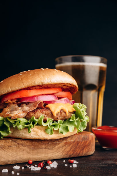 黑色背景的外卖汉堡配脆培根、土豆薯条和一杯啤酒图片下载