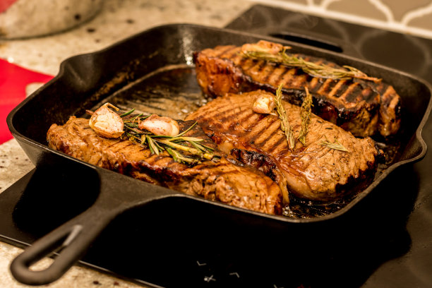 用迷迭香和大蒜在铸铁烤架上烤纽约西冷牛排，在家里的电炉台面上烤图片下载