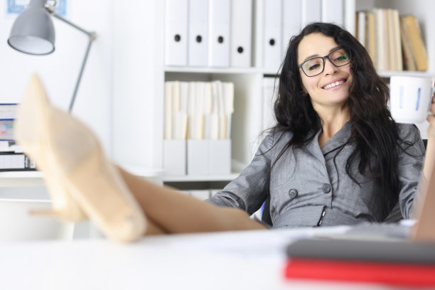 手里拿着杯子的女商人把脚放在办公室的桌子上图片下载