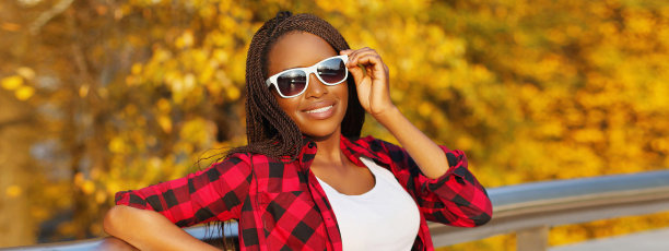 年轻微笑的非洲妇女肖像与脏辫戴墨镜在秋天的公园图片下载