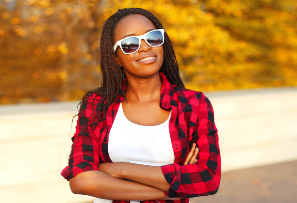 年轻微笑的非洲妇女肖像与脏辫戴墨镜在秋天的公园图片下载