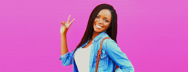 幸福微笑的年轻非洲妇女的肖像与背包在粉红色的背景图片下载