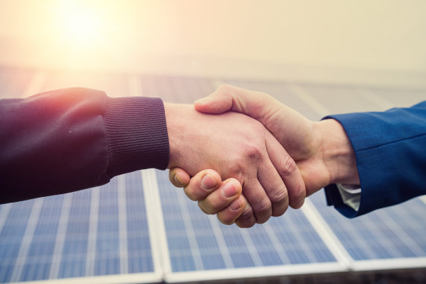 两名穿着工作服、戴着头盔的工人在完成一个面板计划后握手。图片下载