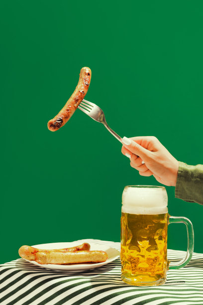 啤酒和炸法兰克福香肠。人的手和一杯冰凉的泡沫啤酒在深绿色的背景。啤酒节，假期，快乐，节日和广告概念。图片下载