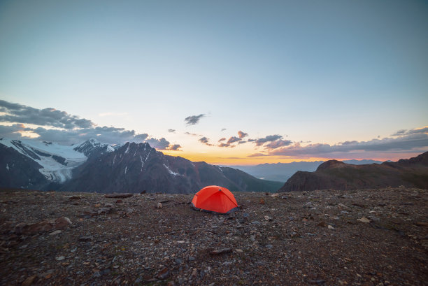 风景优美的高山景观，帐篷在非常高的海拔，在橙色的黎明天空中可以看到大山。生动的橙色帐篷与令人敬畏的看法高山脉下多云的天空在日落的颜色。图片下载