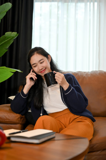 漂亮的亚洲女性在客厅里一边喝咖啡一边打电话放松图片下载
