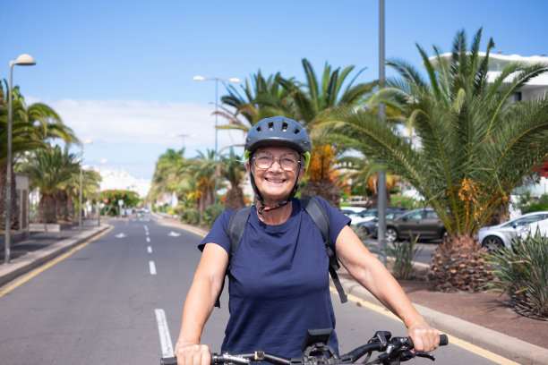 快乐迷人的退休高级妇女与头盔和背包享受活动与电动自行车在城市街道-可持续移动的概念图片下载