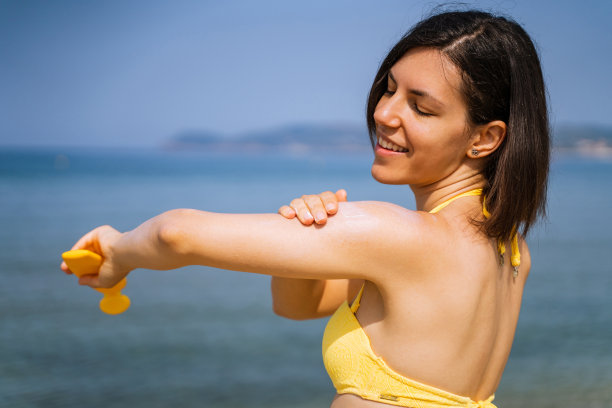 在海滩上涂防晒霜的女人图片下载