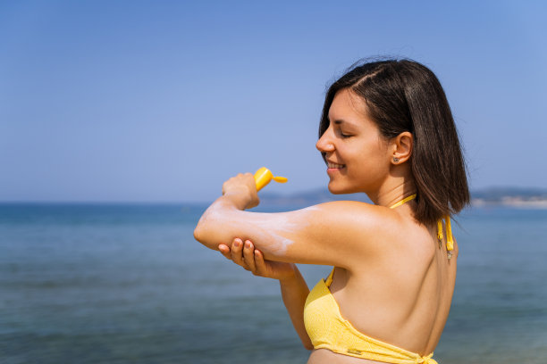 在海滩上涂防晒霜的女人图片下载