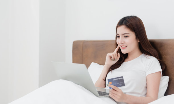 亚洲美女使用信用卡通过互联网使用电脑购物，脸上带着快乐的微笑，成为一种新的常态，在网上购物的经验，从家里。图片下载