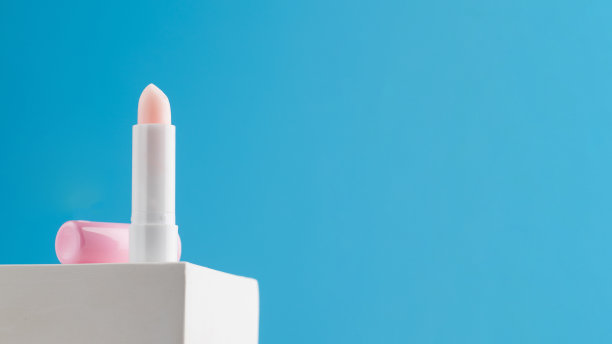 粉红色保湿卫生口红在讲台上的蓝色背景。广告的地方。图片下载
