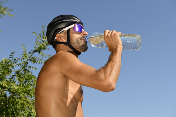铁人三项运动员用他的瓶子喝水，戴着墨镜，没穿衣服。图片下载