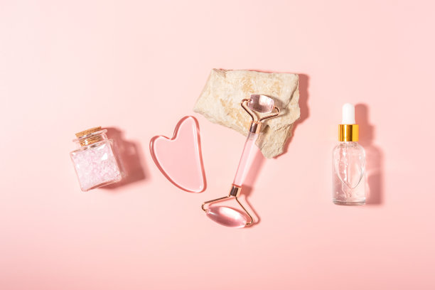 粉色石英石滚筒面部按摩水粉与玻璃化妆瓶粉彩粉底。家庭水疗护理理念，美丽青春，抗衰老。前视图。平的。图片下载