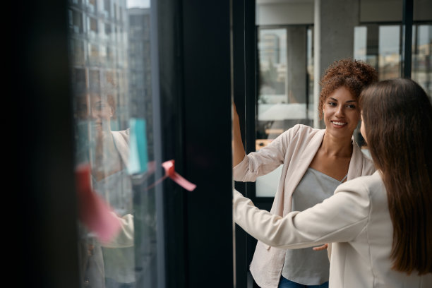 微笑的女商人看着贴着贴纸的窗户。共同办公业务图片下载
