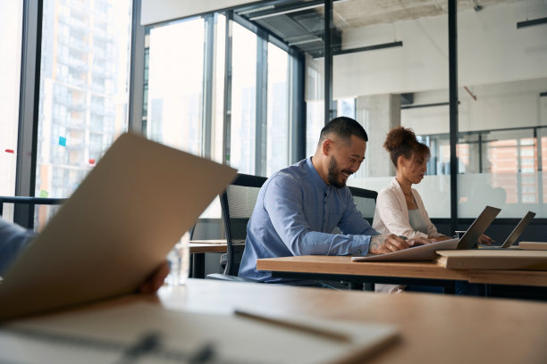 在开放式办公室工作的员工坐在笔记本电脑前的照片图片下载