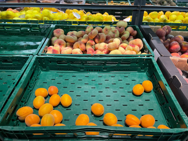 新鲜的杏和桃水果装在一个半空的绿色塑料超市盒子里。蔬菜店图片下载