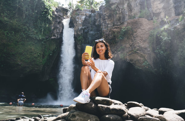 愉快的女性游客在瀑布附近自拍图片下载