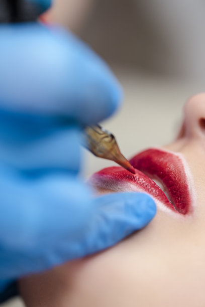 纹身的生活方式的想法。白种女人有永久的嘴唇化妆在美容院期间永久化妆纹身而画轮廓与特殊的工具。图片下载