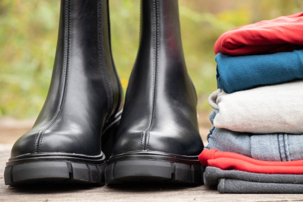 街上晒着太阳的木板上站着厚底的女式黑色高筒靴和一堆东西，还有女鞋和冬装、时髦的衣服和鞋子图片下载