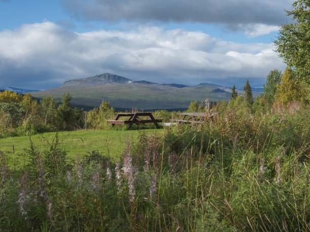 木制野餐桌，可以看到瑞典拉普兰Kvikkjokk的萨瑞克山的美丽风景。夏日艳阳天，黄金时辰，风云变幻图片下载