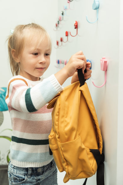 可爱的白人小女孩把黄色的背包挂在学校更衣室的白色衣架上。回归学校理念图片下载