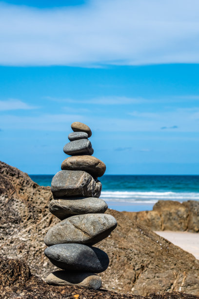 一座石塔矗立在蓝天下的岩石海滩上图片下载
