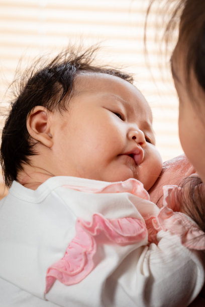 一个新生儿女婴靠在妈妈的肩膀上睡觉，妈妈抱着她，用她的爱和温暖安慰她睡觉。亚洲单身妈妈哄女儿睡觉图片下载
