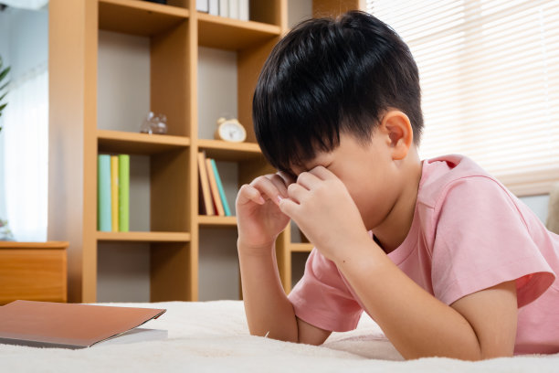 一个亚洲男孩，英俊，躺在他最喜欢的柔软的床上看书，他把书放在床上，用双手揉眼睛，阅读的无聊使他昏昏欲睡。图片下载