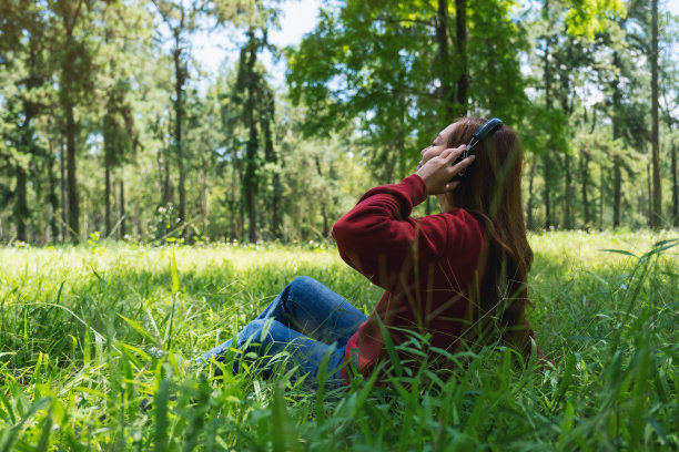 一个美丽的年轻亚洲女人的肖像享受听音乐与耳机坐在公园图片下载