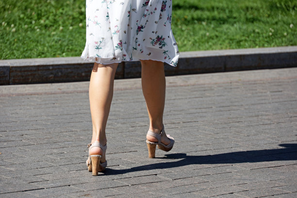 穿着夏天裙子的女人的腿和高跟鞋走在城市的街道上图片下载