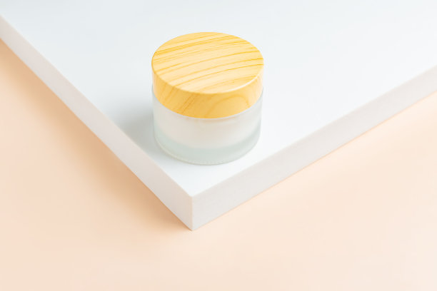 用于彩妆面霜产品展示的单色场景。米色背景上白色底座上的竹盖化妆品罐。图片下载