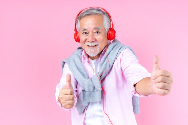 老年老人微笑着戴着红色耳机，幸福的亚洲老人听着音乐跳着粉色的背景舞。图片下载