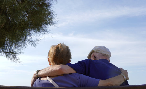 一对老夫妇从后面互相拥抱。蓝色的天空背景图片下载