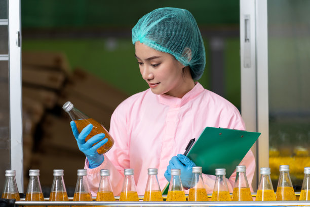 在饮料厂检查输送带上产品瓶子的女工。生产和检验质量控制图片下载