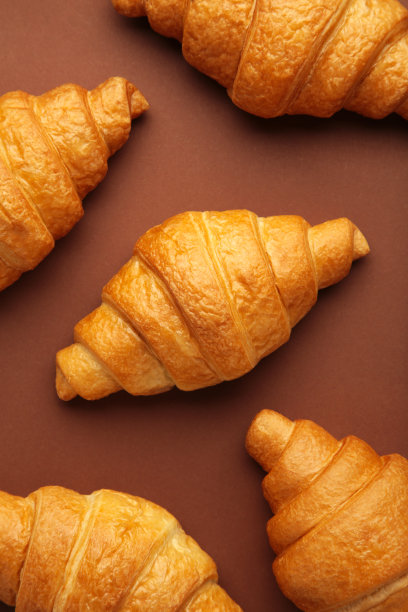 新鲜出炉的牛角面包在棕色的木制背景温暖新鲜的黄油牛角面包和面包卷。法式和美式牛角面包和烘焙糕点。垂直的照片。图片下载