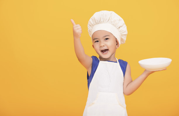 穿着厨师制服的快乐男孩在黄色背景上竖起大拇指图片下载
