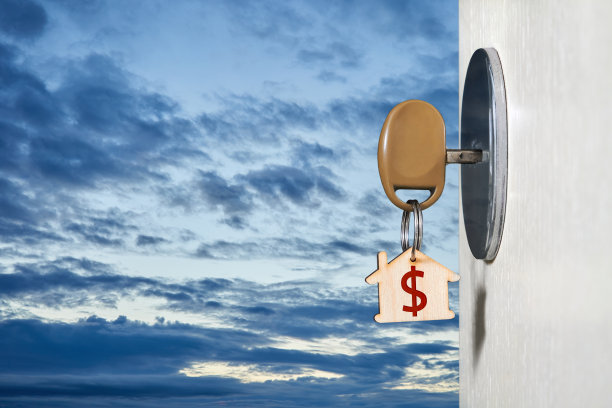 钥匙与一个小饰品的形式在一个房子的门锁上的一扇开着的门，背景是天空与云彩图片下载