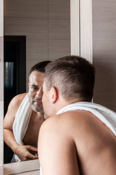 一个男人肩膀上搭着一条毛巾，在家里的浴室里仔细地看着镜子图片下载