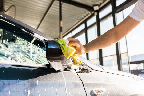 一名男子在自助洗车店用泡沫擦洗自己车上的镜子图片下载