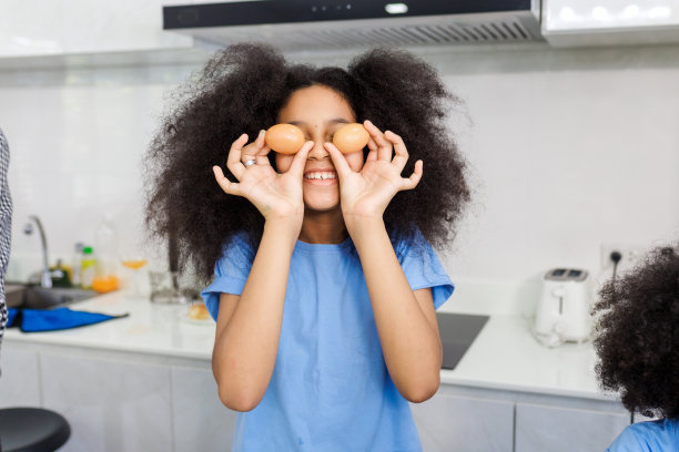 孩子拿着鸡蛋在他的眼睛附近，在厨房做饭。孩子们娱乐。健康饮食的概念图片下载