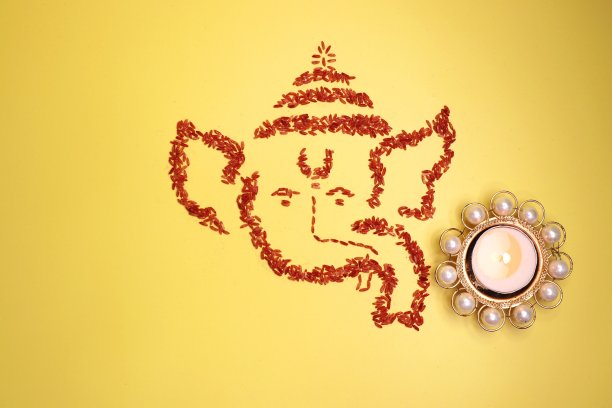 象头神是用彩色大米制作的。象头神墙纸或旗帜。甘帕蒂脸在黄色的背景随着diya和花。副本的空间。图片下载