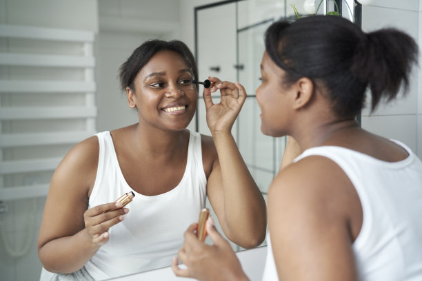 微笑的非洲裔美国女性在浴室镜子前画睫毛图片下载