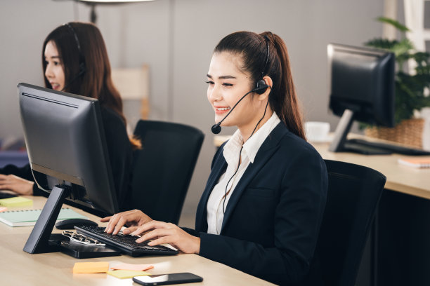 年轻的商业人员亚洲女性工作与耳机和电脑的支持。图片下载