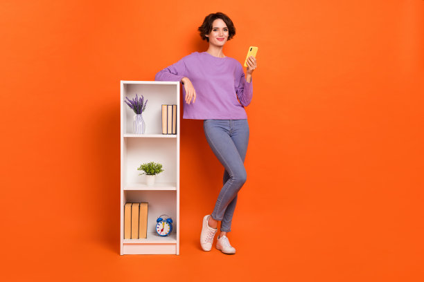 全身照片可爱漂亮的女孩穿着紫色套头衫打字装置书架孤立的橙色背景图片下载